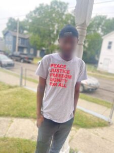 A man stands outside a home in Hamilton, Ohio, wearing a shirt he got from ICE as he was released from custody. He and hundreds like him are preparing to file for asylum in the US due to apartheid and slavery in Mauritania. (Photo credit: Ohio Immigrant Alliance © 2023)